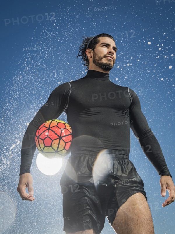 Water splashing on Hispanic man holding soccer ball