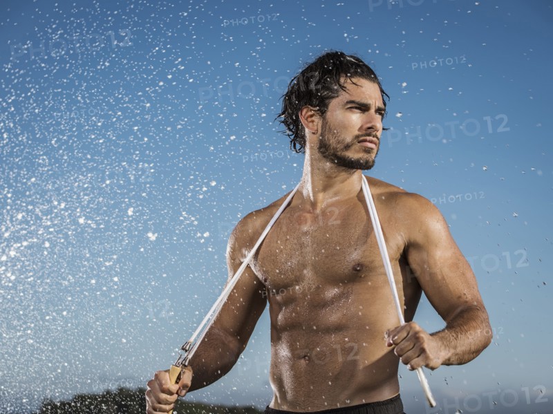 Water splashing on Hispanic man holding jump rope