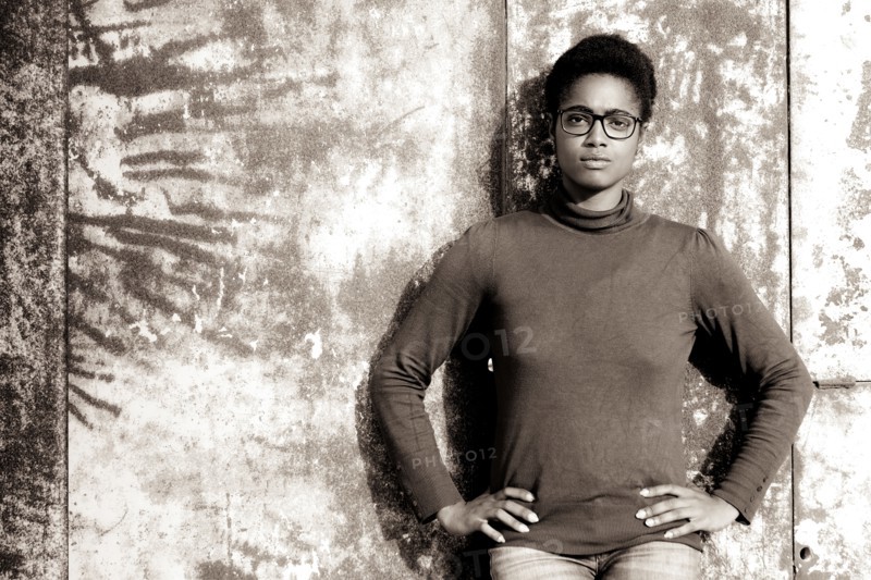 Serious African American woman leaning on rusty metal wall