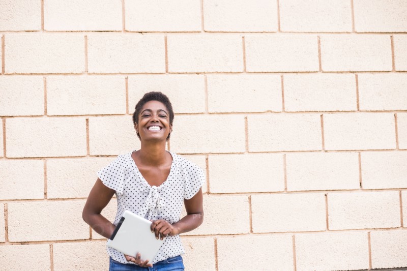 Smiling African American woman holding digital tablet near concrete wall