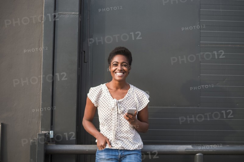 Smiling African American woman leaning on railing texting on cell phone