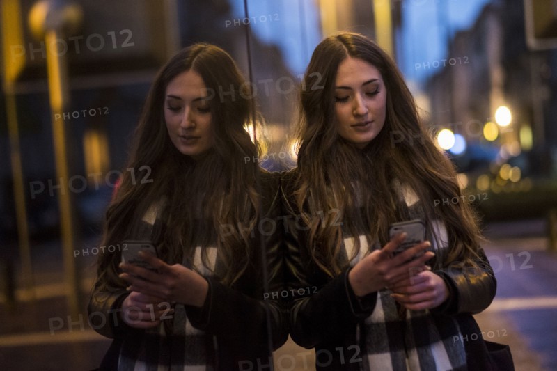 Caucasian woman leaning on window texting on cell phone outdoors