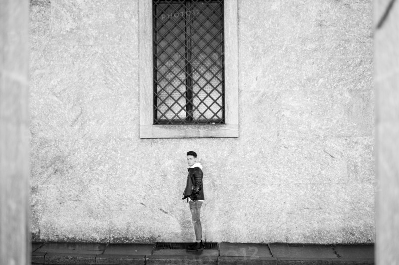 Portrait of distant man standing underneath window on sidewalk