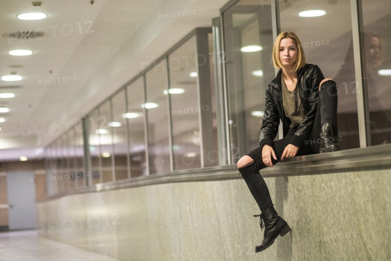 Caucasian woman sitting on ledge of window in corridor
