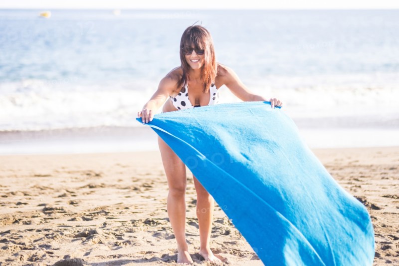 Caucasian woman spreading blanket on beach