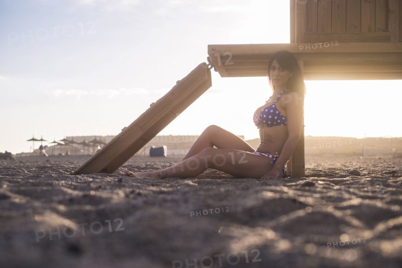 Caucasian woman sitting on beach leaning on cabana