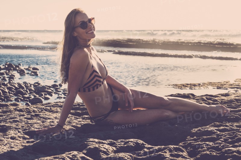 Caucasian woman sitting on beach wearing bikini