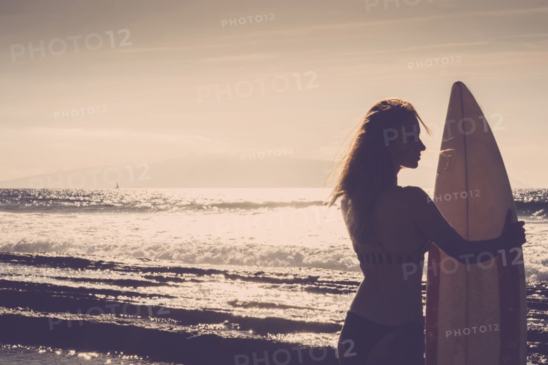 Caucasian woman standing on beach holding surfboard