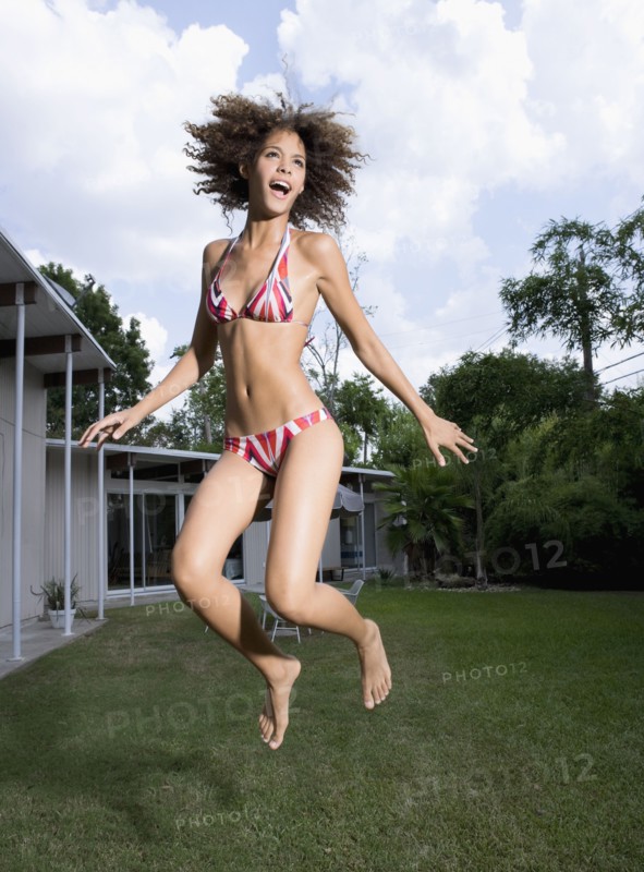 Mixed race woman in bikini jumping in backyard