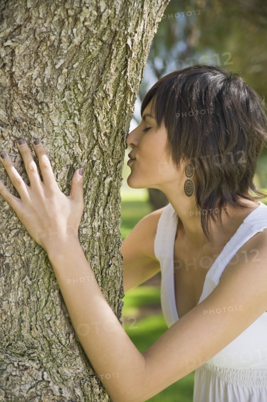 Hispanic woman hugging tree trunk