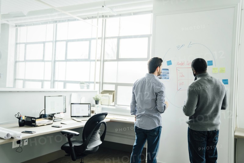 Businessmen using whiteboard in office