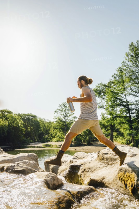 Caucasian man jumping on rocks near river