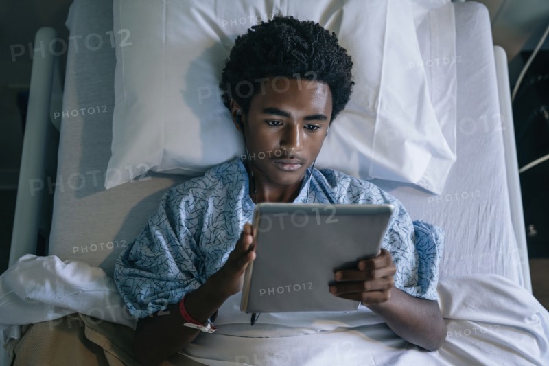 Black boy in hospital bed listening to digital tablet