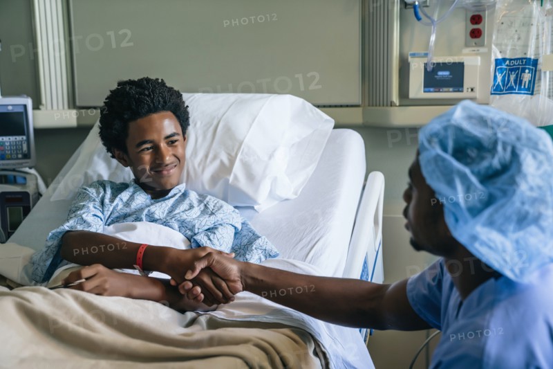 Black nurse shaking hands with boy in hospital bed