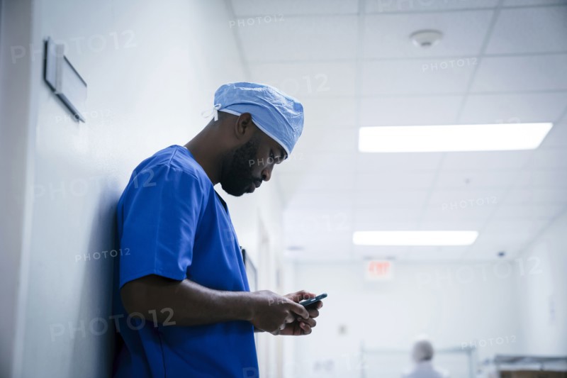 Black nurse leaning on wall texting on cell phone
