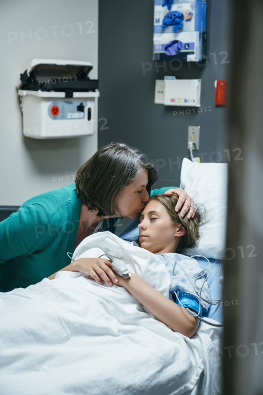 Mother kissing forehead of daughter in hospital bed