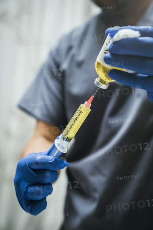 Mixed race nurse wearing rubber-gloves holding medicine and needle
