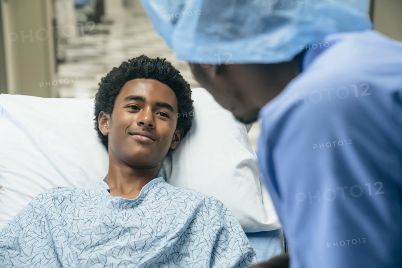 Black doctor talking to boy in hospital bed