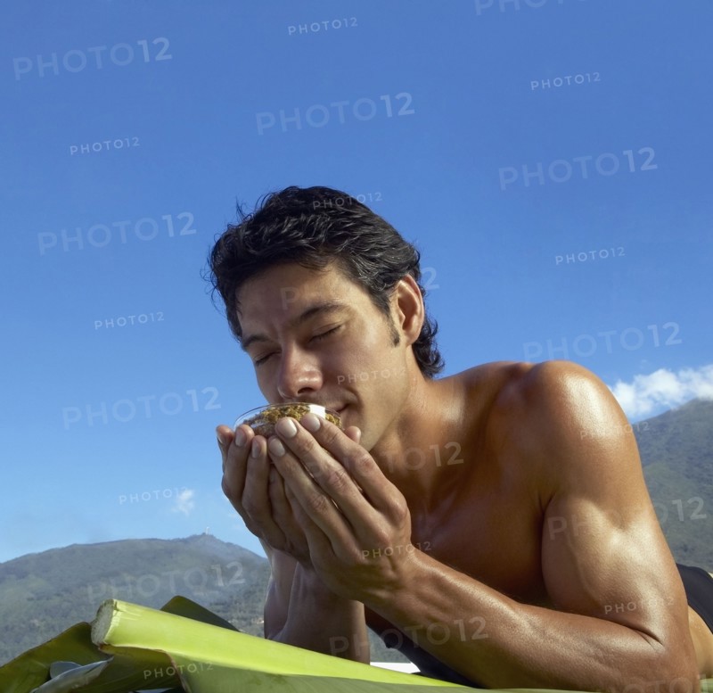 Low angle view of Asian man laying on banana leaves and smelling bowl of botanical medicine