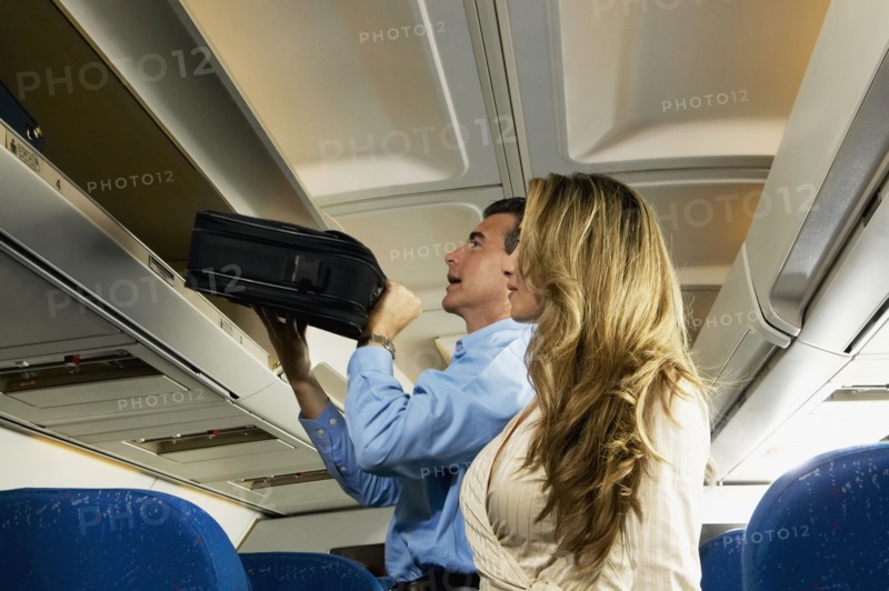 Couple stowing luggage in overhead compartment on airplane