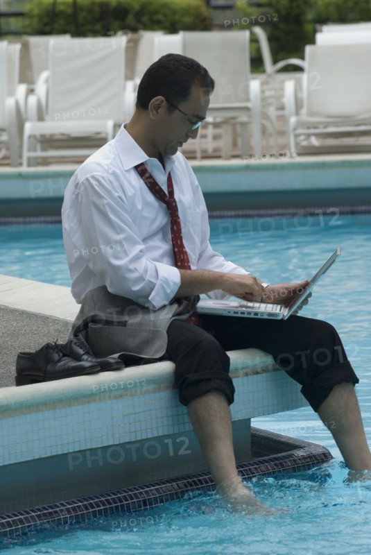 Hispanic businessman using laptop next to swimming pool