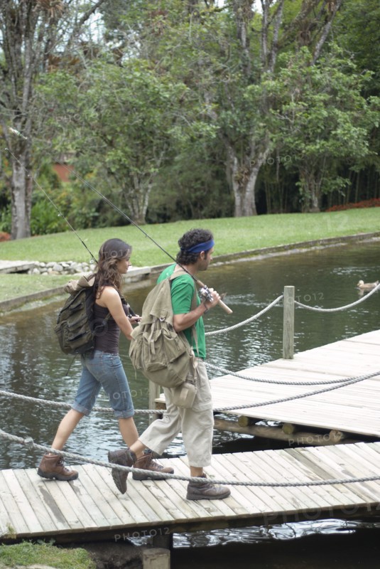 Hispanic couple walking on pier carrying fishing poles