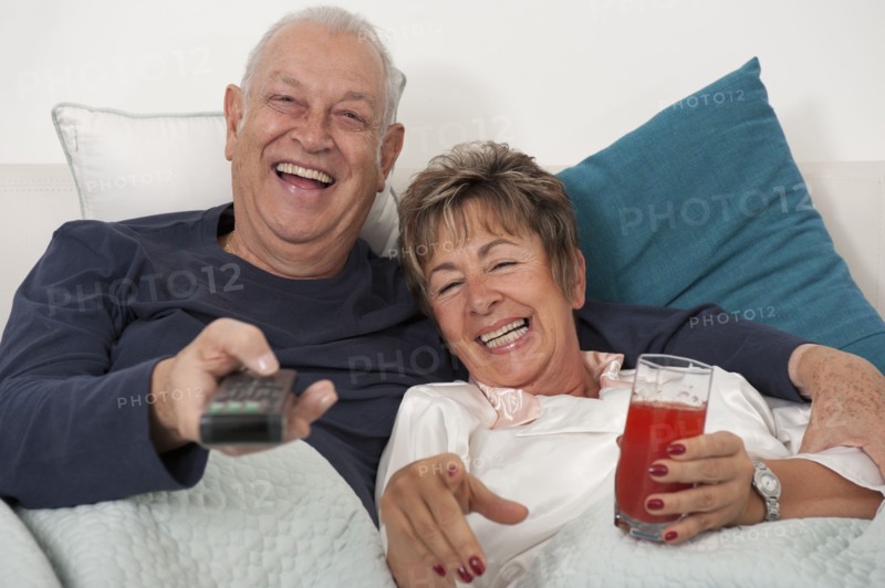 Senior Hispanic couple laying in bed watching television
