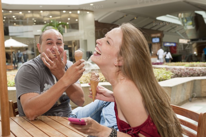 Laughing Hispanic couple eating ice cream cones in cafe