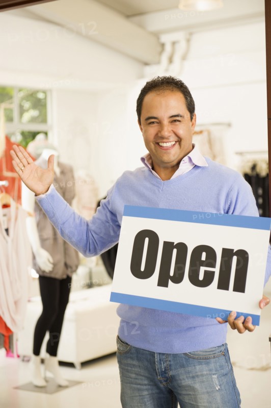 Hispanic man holding open sign in clothing store