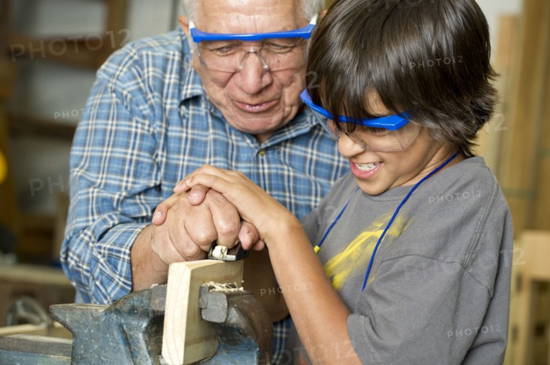 Hispanic grandfather and son planing wood in workshop