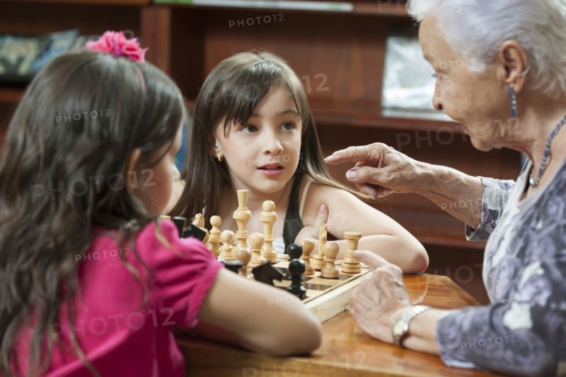 Hispanic grandmother and granddaughters playing chess