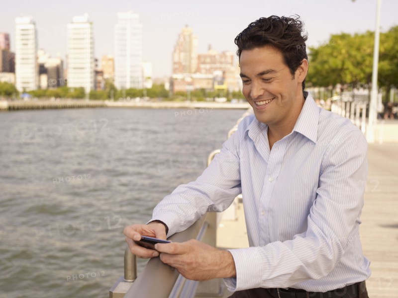 Man at waterfront text messaging on cell phone