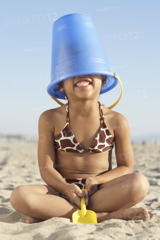 Young mixed race girl with bucket on head at beach