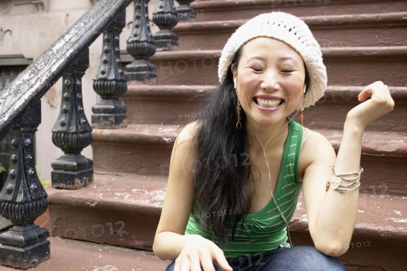 Asian woman sitting on front steps listening to music