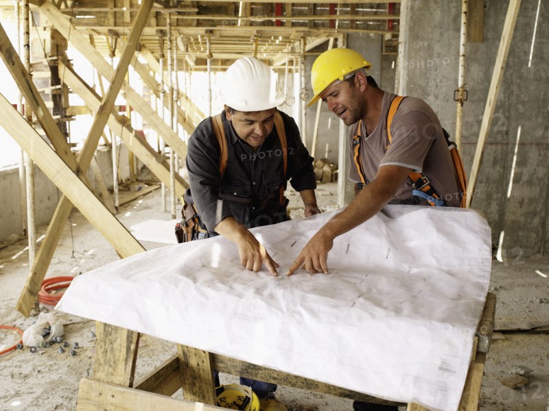 Hispanic workers looking at blueprints on construction site
