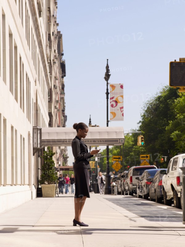 African businesswoman looking at cell phone on sidewalk