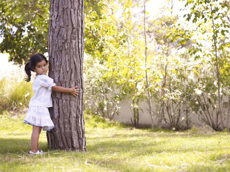 Hispanic girl hugging tree trunk
