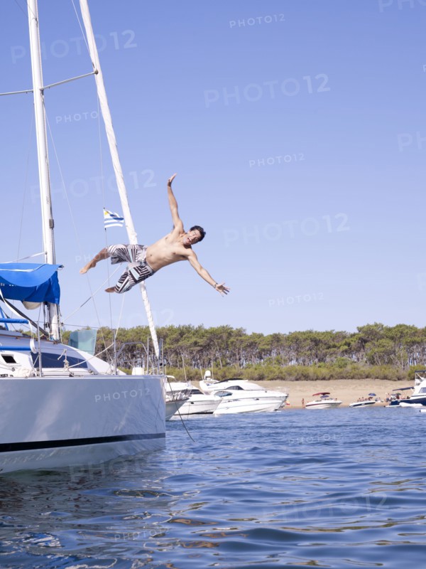 Hispanic man jumping into ocean from sailboat