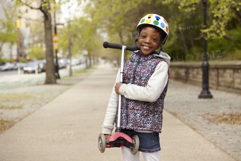 Mixed race girl holding push scooter on sidewalk