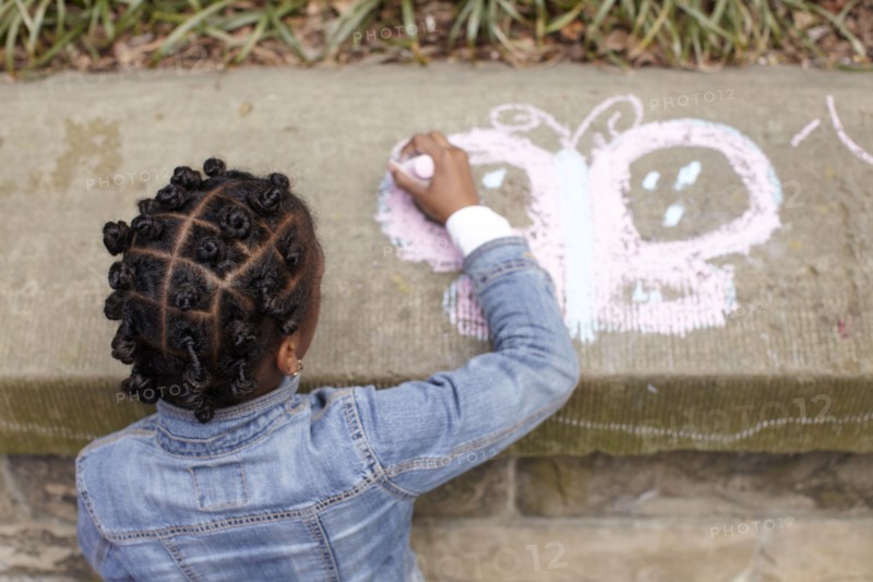 Mixed race girl drawing on cement with chalk