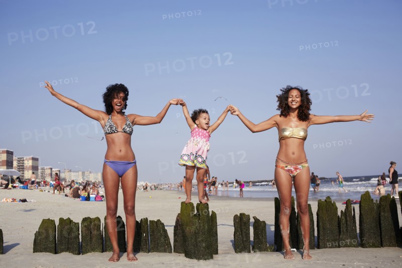 Mixed race women and girl holding hands at beach