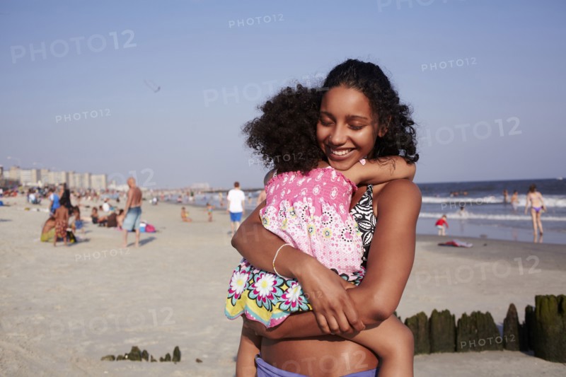 Mixed race mother and daughter hugging at the beach
