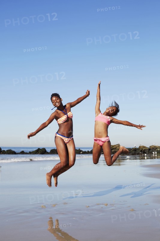 Black women jumping for joy on beach