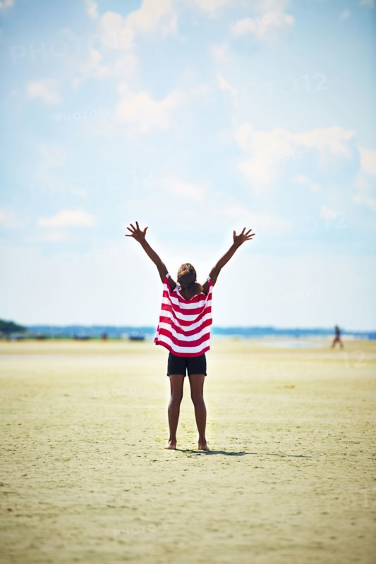 Black girl standing with arms raised on beach