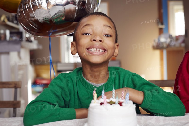 Black boy smiling with balloon and cake at party