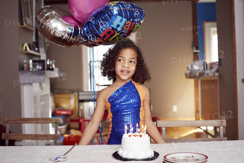 Mixed race girl with balloons and cake at party