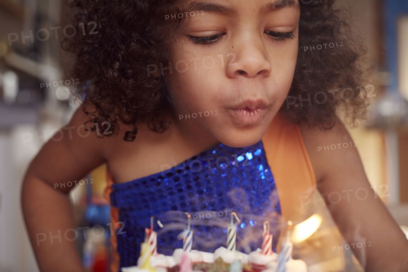 Mixed race girl blowing out cake candles