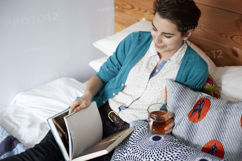 Woman drinking tea and reading in bed