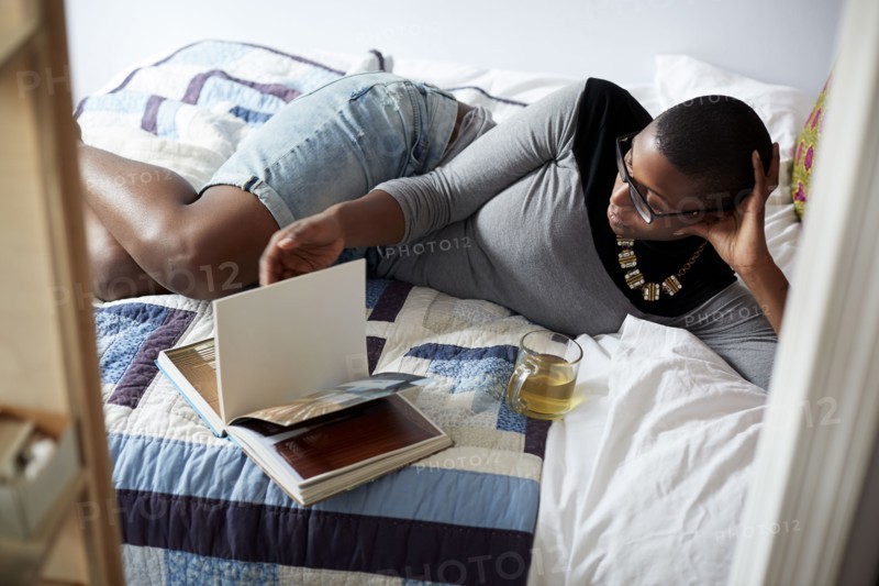 Mixed race woman drinking tea and reading on bed