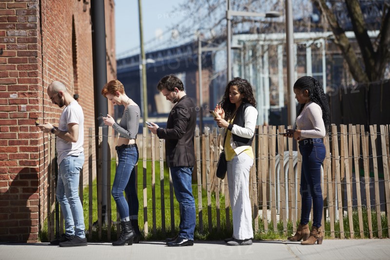 People in line on sidewalk using cell phones
